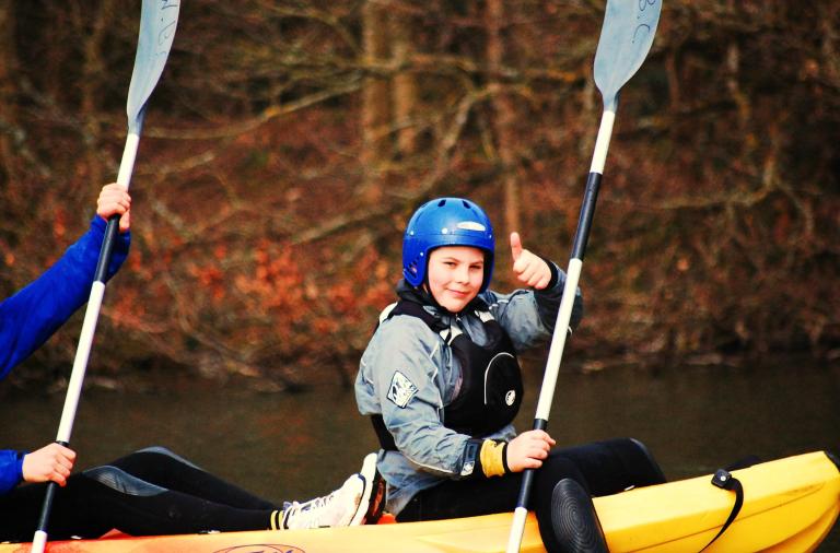 a kid giving a thumbs up on a double kayak